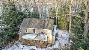 A two-story house with a porch, surrounded by trees and a snowy ground.