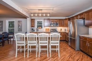 A modern kitchen with wooden cabinets, a stainless steel refrigerator, and a dining area with white chairs.