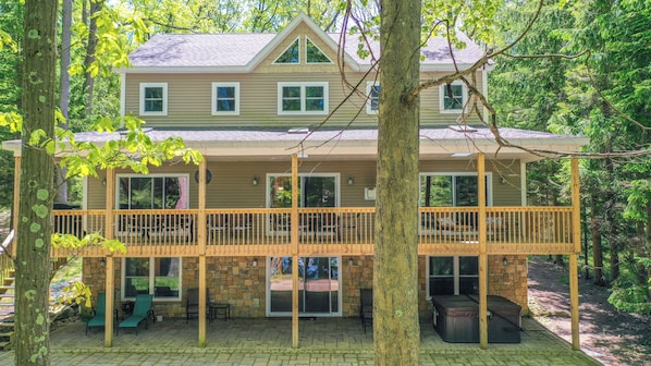 A two-story house with a stone foundation, a wooden deck, and a covered patio area.