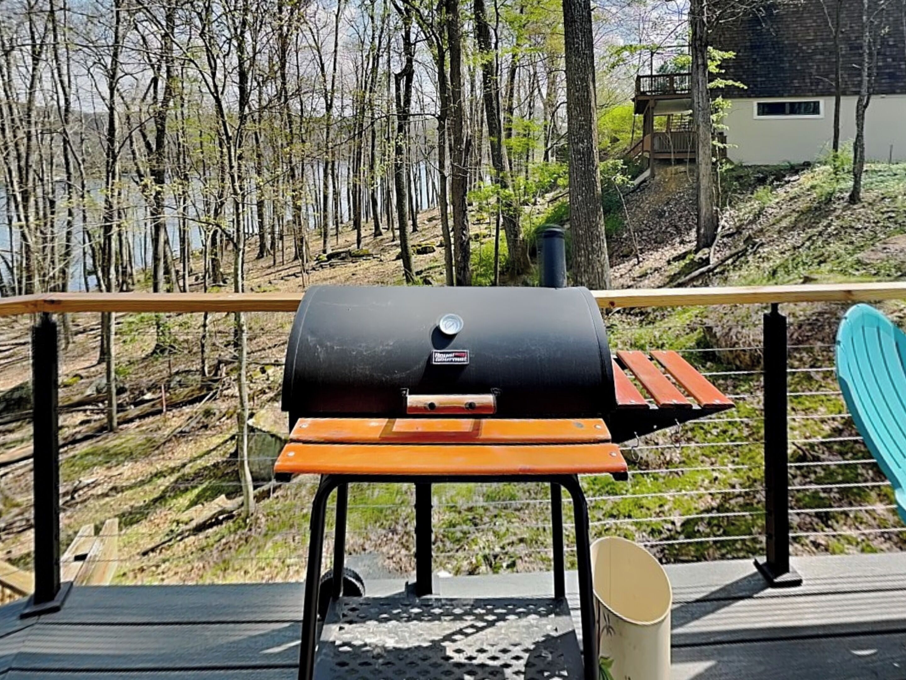 Una parrilla de barbacoa en una terraza con vistas a un bosque y una casa al fondo.