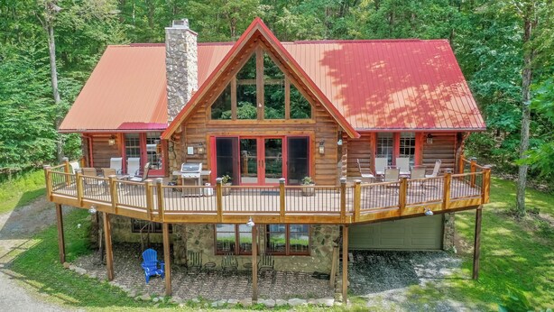 A log cabin with a deck, outdoor seating, and a stone chimney.