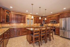 A spacious kitchen with wooden cabinets, a stainless steel refrigerator, and a large island with bar stools. - Rockledge Manor by Taylor Made Deep Creek (McHenry)