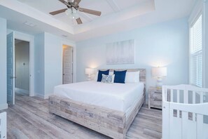 Une chambre à coucher avec un lit en bois, un ventilateur de plafond et un berceau blanc.
