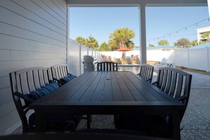 Un espace extérieur abrité, aménagé pour les repas, avec une longue table et des chaises, un barbecue et une piscine en arrière-plan.