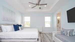 A bedroom with a wooden bed frame, white bedding, and a ceiling fan. - Sandy of Panama City Beach - Ocean View, Heated Pool, Steps to Beach, Sleeps 18 (Panama City Beach)