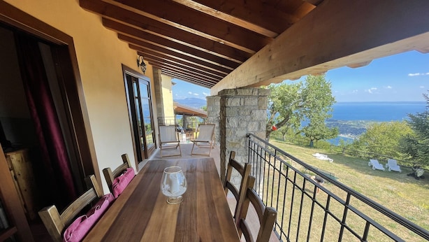 Una mesa de madera con sillas, un vaso de agua y vistas al mar y al paisaje.