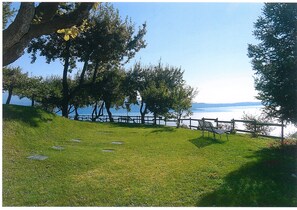 A grassy park area with a bench and a wooden fence overlooking a body of water.