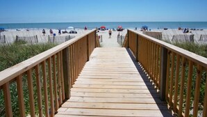 A wooden boardwalk leading to a beach with people and umbrellas.