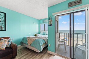 Ein Schlafzimmer mit Bett, Stuhl, Fenster und Blick auf den Strand.