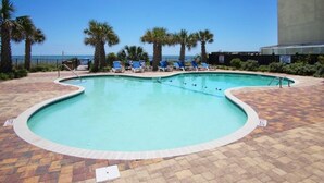 A swimming pool with lounge chairs and palm trees, surrounded by a brick patio.