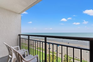 A balcony with a view of a beach, a railing, and two chairs.