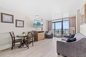 A modern living room with a dining area, a flat-screen TV, and a balcony with a view.