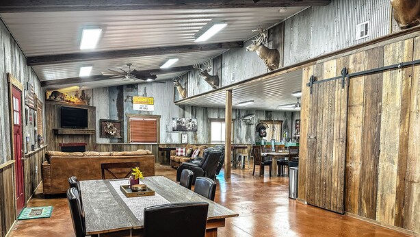 Een rustiek interieur met een houten eettafel, stoelen, een bank en een aan de muur bevestigde televisie.