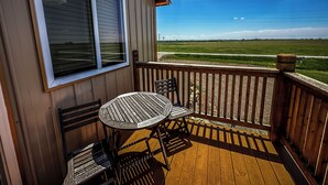 Een houten terras met een tafel, stoelen, een raam en uitzicht op een groen veld.