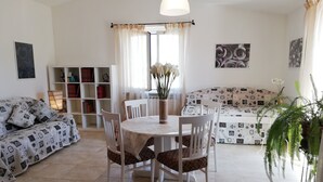 Una sala de estar con una mesa de comedor, sillas, un sofá y una estantería.