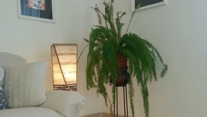 Una sala de estar con un sofá, un helecho en maceta, una lámpara de pared y cuadros enmarcados.