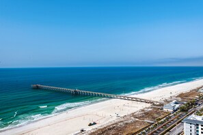 Ein Strand mit einer langen Pier, die sich ins Meer erstreckt, feinem Sand und angrenzenden Gebäuden.