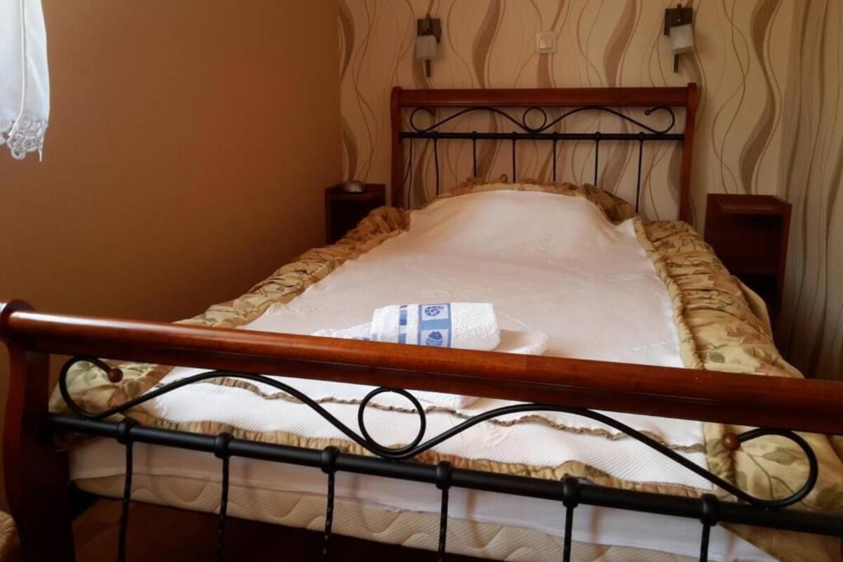 Ein Bett mit Holz-Kopfstück, einem weißen Kopfkissen und einer gemusterten Bettdecke.