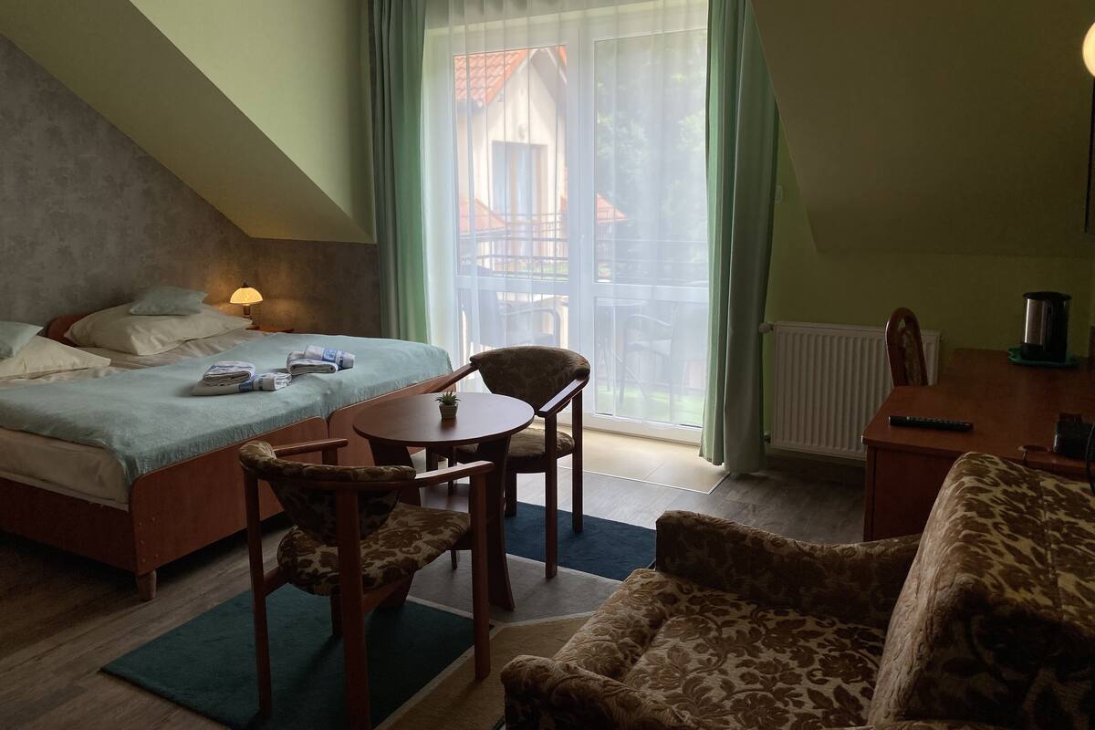 Ein Hotelzimmer mit Bett, einem kleinen Tisch, zwei Stühlen, einer Heizung und einem Fenster mit Vorhängen.