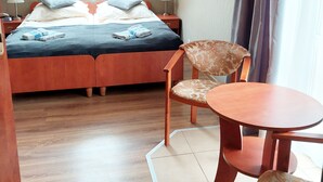 Un dormitorio con cama, dos mesitas de noche, una silla, una pequeña mesa y una ventana con cortinas.