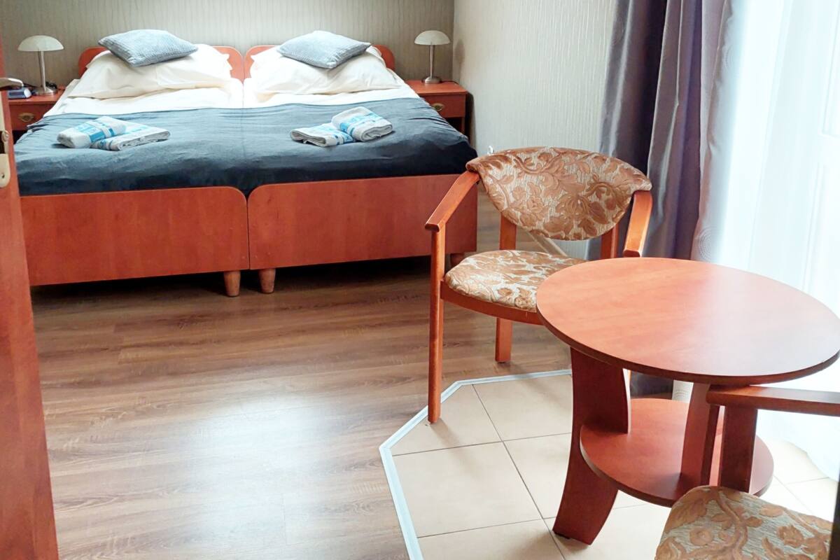 Ein Schlafzimmer mit einem Bett, zwei Nachttischen, einem Sessel, einem kleinen Tisch und einem Fenster mit Vorhängen.