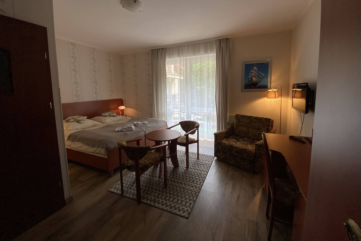 Ein Hotelzimmer mit Bett, Schreibtisch, Stuhl, Tisch, Lampe und einem Bild an der Wand.