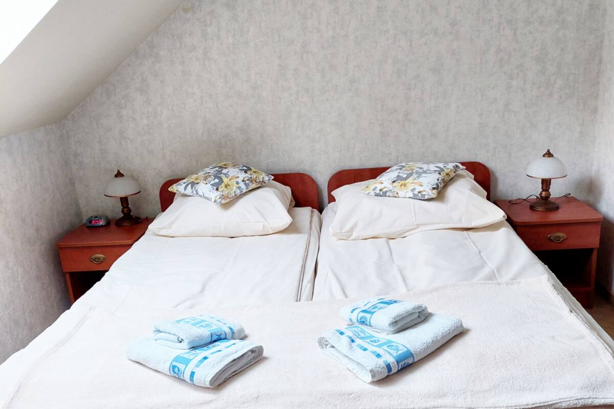 Ein Doppelbett mit weißen Laken und blauen Handtüchern, zwei Nachttische mit Lampen sowie ein roter, gepolsterter Sessel.