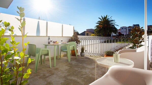A patio area with a table and chairs, a potted plant, and a view of the surrounding buildings.