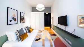 Et moderne hotelværelse med sofa, kunstværker, et fjernsyn og en gang, der fører til en dør.
