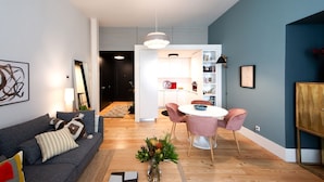 En moderne stue med en grå sofa, et rundt bord med pink farvede stole og et bogreol.