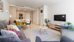 A modern living room with a grey sofa, a yellow dining table, and a TV on the wall.