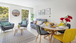 A modern living room with a grey sofa, two armchairs, a coffee table, and a dining table set for breakfast.