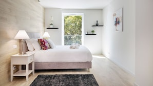 A modern bedroom with a bed, bedside tables, a window with a view of trees, and minimalist decor.
