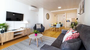Un salon moderne doté d’un téléviseur à écran plat, d’un canapé gris, d’une table basse et d’un coin repas avec une petite table ronde et des chaises.