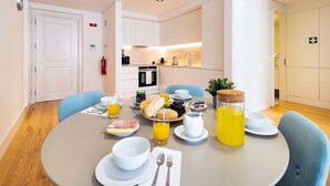 Une table mise pour le petit-déjeuner, avec une nappe et de la vaisselle pour deux personnes, comprenant des assiettes, des bols, des couverts et divers aliments pour le petit-déjeuner, comme du pain, des fruits et du jus.