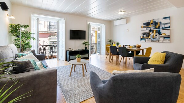 Ein modernes Wohnzimmer mit einer Couch, Sesseln, einem Couchtisch und einem Essbereich mit Stühlen und Tisch.