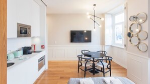 A modern kitchen with a microwave, toaster, and kettle, a dining area with a table and chairs, and a TV mounted on the wall. - Cute & Bright Flat w/ AC by LovelyStay (Porto)