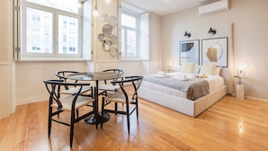 A modern bedroom with a bed, bedside tables, and a dining area with a table and chairs. - Cute & Bright Flat w/ AC by LovelyStay (Porto)