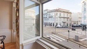 A view from a window overlooking a street with buildings, a pedestrian crossing, and parked cars. - Cute & Bright Flat w/ AC by LovelyStay (Porto)