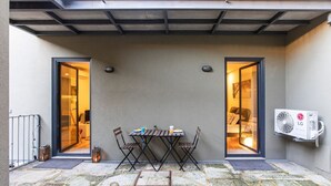 A small patio area with a table and chairs, two doors leading to a room, and an air conditioning unit mounted on the wall. - Downtown Studio w/ AC & Patio by LovelyStay (Porto)