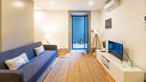 A modern living room with a sofa, a TV, and a small table. - Downtown Studio w/ AC & Patio by LovelyStay (Porto)