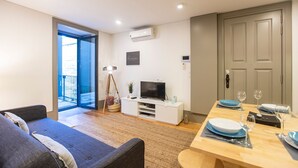 A modern living room with a sofa, a TV, a dining table set for two, and a balcony door. - Downtown Studio w/ AC & Patio by LovelyStay (Porto)