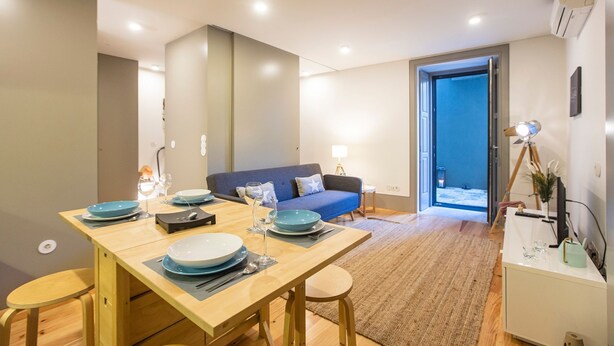 A modern living room with a dining area, a sofa, and a view of the outside. - Downtown Studio w/ AC & Patio by LovelyStay (Porto)