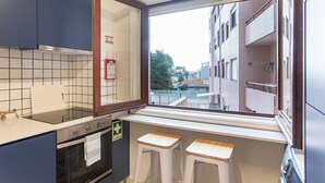 A compact kitchen with a window, a stove, and two stools. - Tasteful 2BR Flat in Art District by LovelyStay (Porto)