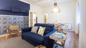 A cozy living area with a blue sofa, a wooden chair, a dining table set for two, and a patterned wall. - Tasteful 2BR Flat in Art District by LovelyStay (Porto)