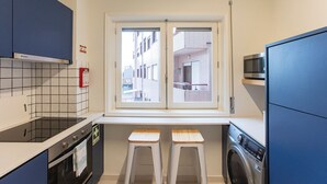 A compact kitchen with a window, a microwave, a washing machine, and a small stool. - Tasteful 2BR Flat in Art District by LovelyStay (Porto)