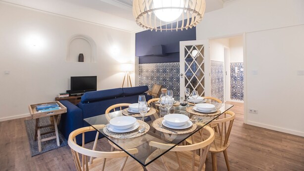 A modern living room with a blue sofa, a glass dining table set for four, and a television on a stand. - Tasteful 2BR Flat in Art District by LovelyStay (Porto)