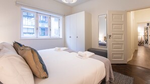 A bedroom with a bed, pillows, a window, a wardrobe, and a door leading to another room. - Tasteful 2BR Flat in Art District by LovelyStay (Porto)