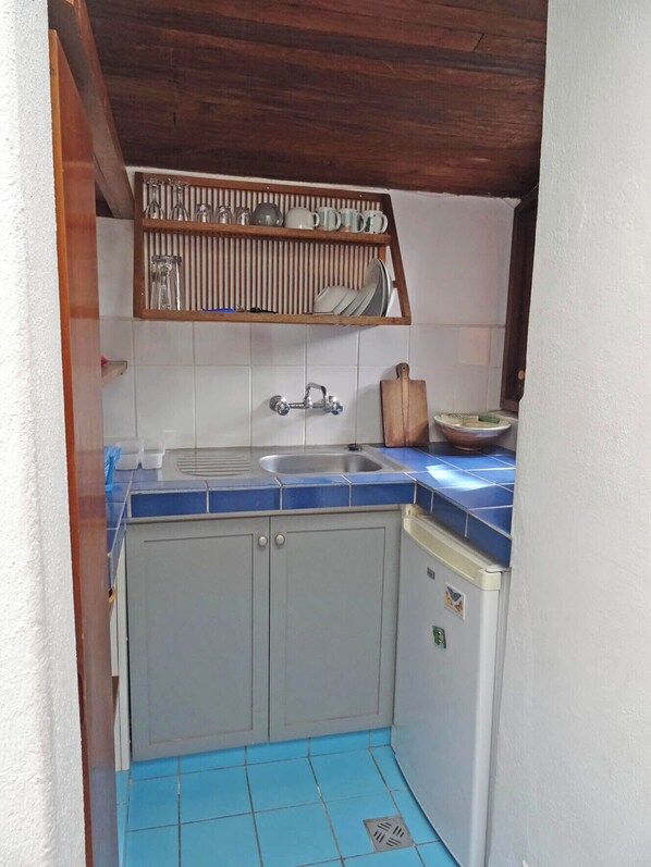 A compact kitchen with a sink, blue-tiled countertop, and a wooden shelf above holding dishes and utensils. - Small cosy house that is an architectural gem in Sopocachi, La Paz, Bolivia (La Paz)