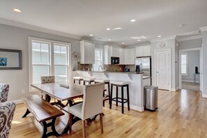A spacious kitchen with white cabinets, a wooden dining table, and a stainless steel trash can.